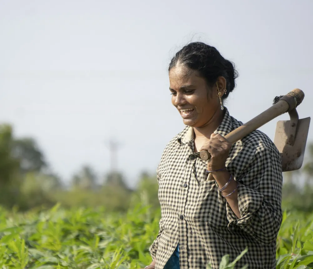A smiling woman farmer with a hoe on her shoulder in a green field