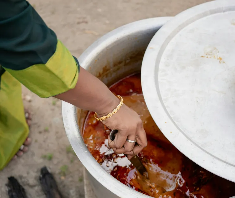 A large pot of curry being stirred over a wood fire